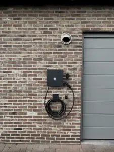 Smappee-laadpaal met kabelhouder naast een garagepoort, geplaatst door Wattra