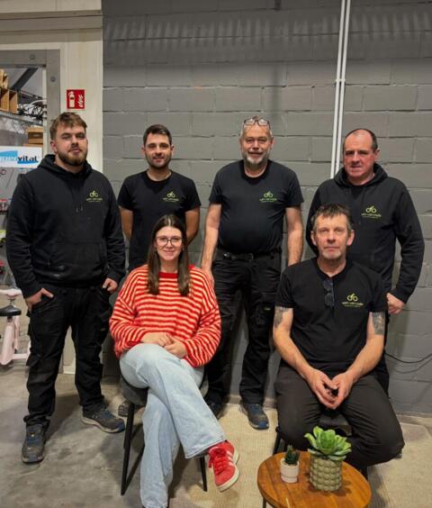Team van zes medewerkers bij fietsenwinkel Fietsen Vervaele in werkruimte met grijze muur