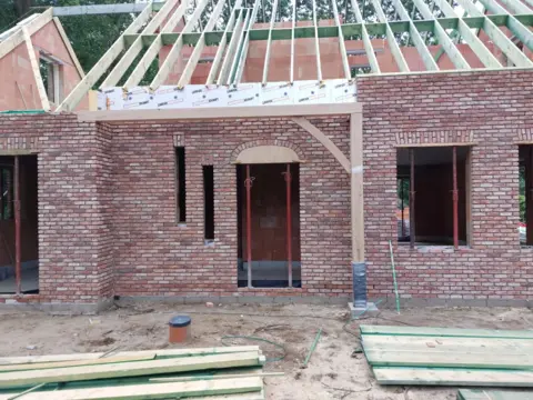 Een gebouw dat in aanbouw is, met een bakstenen muur en houten balken voor het dak.