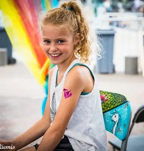Een meisje met een gepersonaliseerde glittertattoo gemaak door Cares'tique