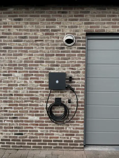 Smappee-laadpaal met kabelhouder naast een garagepoort, geplaatst door Wattra