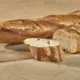 Verse ambachtelijke baguettes met goudbruine, knapperige korst op een houten plank, één in stukken gebroken met luchtige, open kruim zichtbaar.
