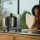 Lachende vrouw houdt een grote bal vers gekneed deeg vast naast de Ooni Halo Pro deegmixer met roestvrijstalen kom op het keukenwerkblad.