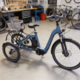 elektrische driewieler met bagagerek en mand in een fietsenwinkel werkplaats met gereedschap en andere fietsen