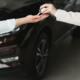 Car sale. Dealer giving key to new owner in auto show or salon, closeup