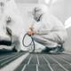 Worker in protective uniform painting car body in paint chamber.