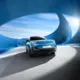 Een blauwe Nissan Micra die door een futuristische tunnel met grote ovale ramen rijdt, met zonlicht aan de zijkant